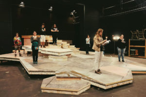 Students stand on a stage reading books aloud