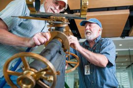 Retired Linfield professor Bill Mackie (left) and Carlton Observatory at Evergreen co-founder Forrest Babcock wrestle with adjustments to a 19th century telescope in preparation for situating the six-inch barrel of the mechanism on its base.