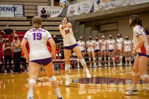 Linfield volleyball player bumps ball to teammate while masked spectators watch