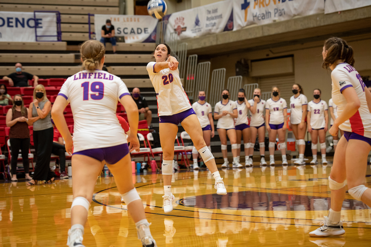 Linfield volleyball player bumps ball to teammate while masked spectators watch