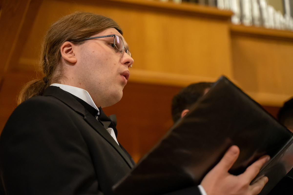 male choral member holds folder and sings