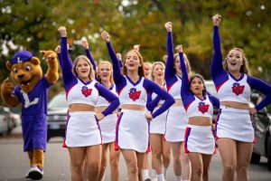 Cheerleaders perform chant with arms raised with mascot in background