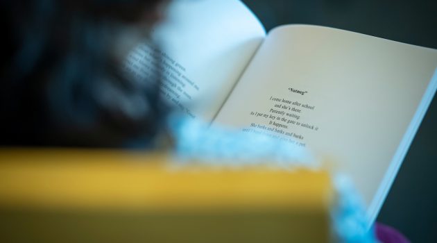 We look over the shoulder of someone with shoulder-length brown hair who is reading a book of poetry.