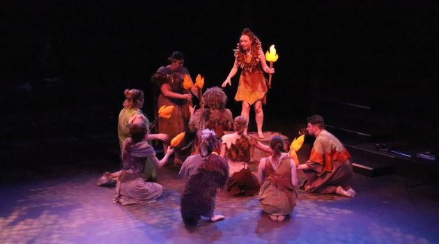 Students are dressed as cave people and holding torches with paper flames during a dress rehearsal for Firebringer.