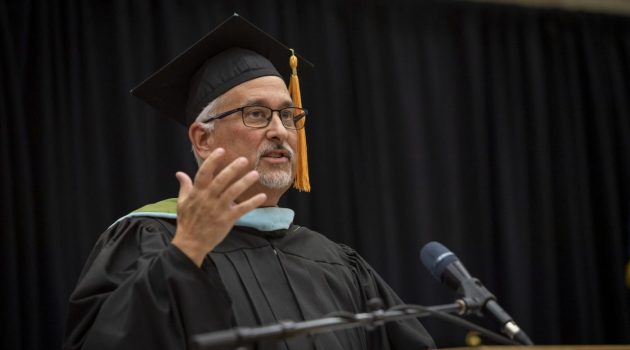 Jeff Mackay gives a speech during convocation wearing academic regalia.