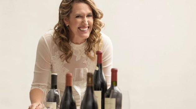 Amanda Wittstrom Higgins leans over a bar cart with wine bottles on top.