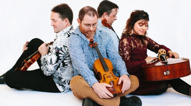 The Pyxis Quartet sits back-to-back with their instruments.