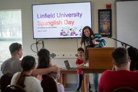A woman and her small son stand in front of a display that says "Linfield University Spanglish Day."