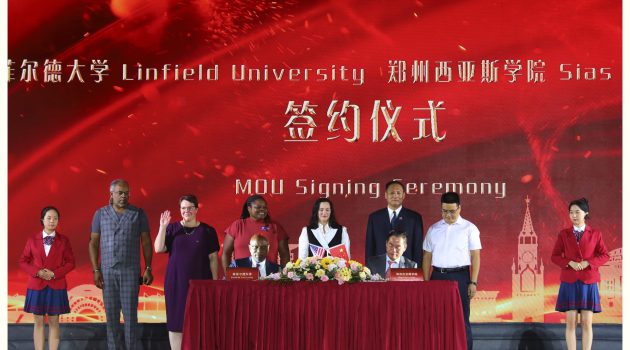 Dean Gennie VanBeek, Dean Jennifer Madden and two delegates of Sias stand behind Miles Davis and Shawn Chen, who are seated at a table strewn with flowers, an American Flag and a Chinese flag.