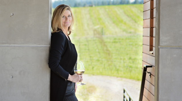 Anna Maria Ponzi stands in a doorway overlooking a vineyard, holding a glass of wine.