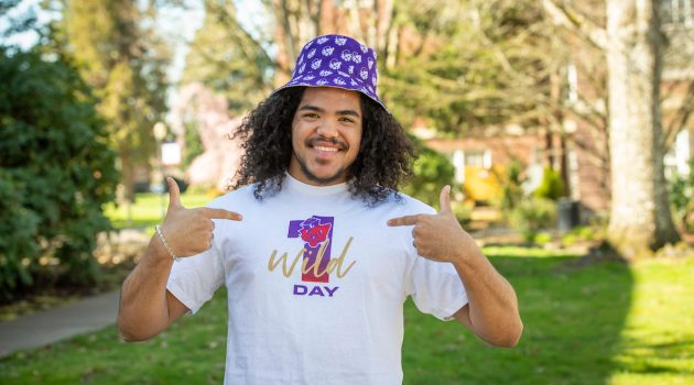 A smiling student wears a Linfield t-shirt and bucket hat