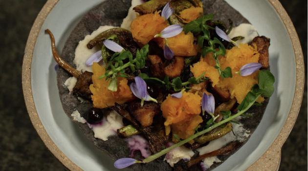 A tostada topped with indigenous foods including squash, foraged watercress and flowers