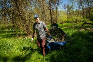 two Linfield community members carry brush out of the Cozine Creek restoration area
