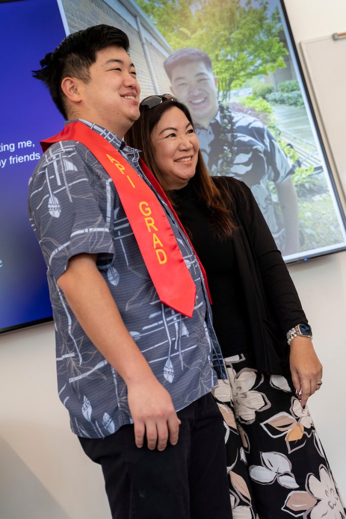 A family embraces during Linfield University’s Asian American-Pacific Islander celebration; the student wears a red stole that says “API Grad”.