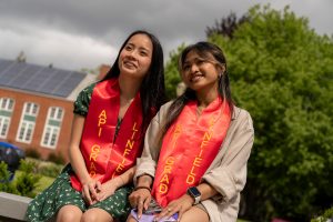 Students pose at Linfield University’s Asian American-Pacific Islander celebration; the students all wears red stoles that says “API Grad”.