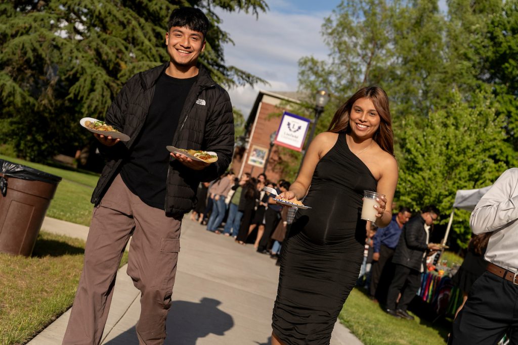 People carry plates of food and smile at the Linfield University Latine Dinner.