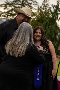A family member places a purple stole that says Linfield Latina around the neck of a graduate during the Linfield University Latine Dinner.