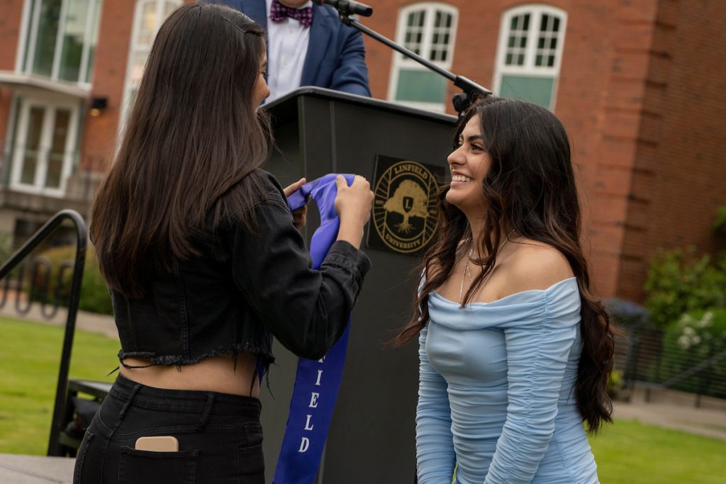 A family member places a purple stole that says Linfield Latina around the neck of a graduate during the Linfield University Latine Dinner.