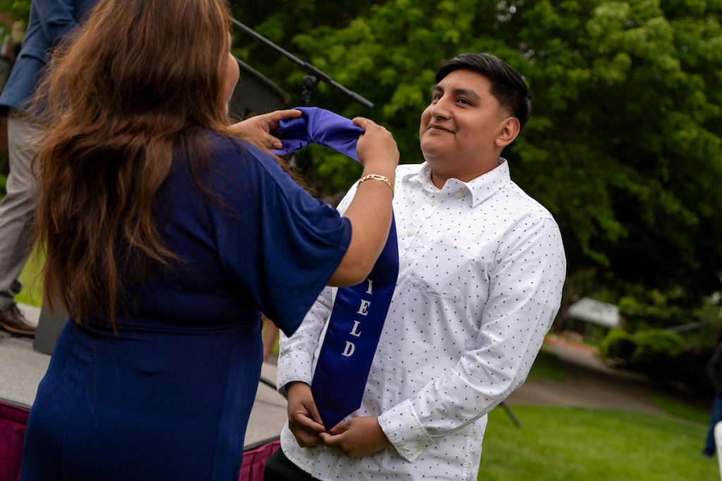 A family member places a purple stole that says Linfield Latino around the neck of a graduate during the Linfield University Latine Dinner.