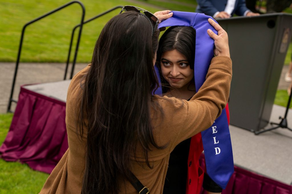 A family member places a purple stole that says Linfield Latina around the neck of a graduate during the Linfield University Latine Dinner.