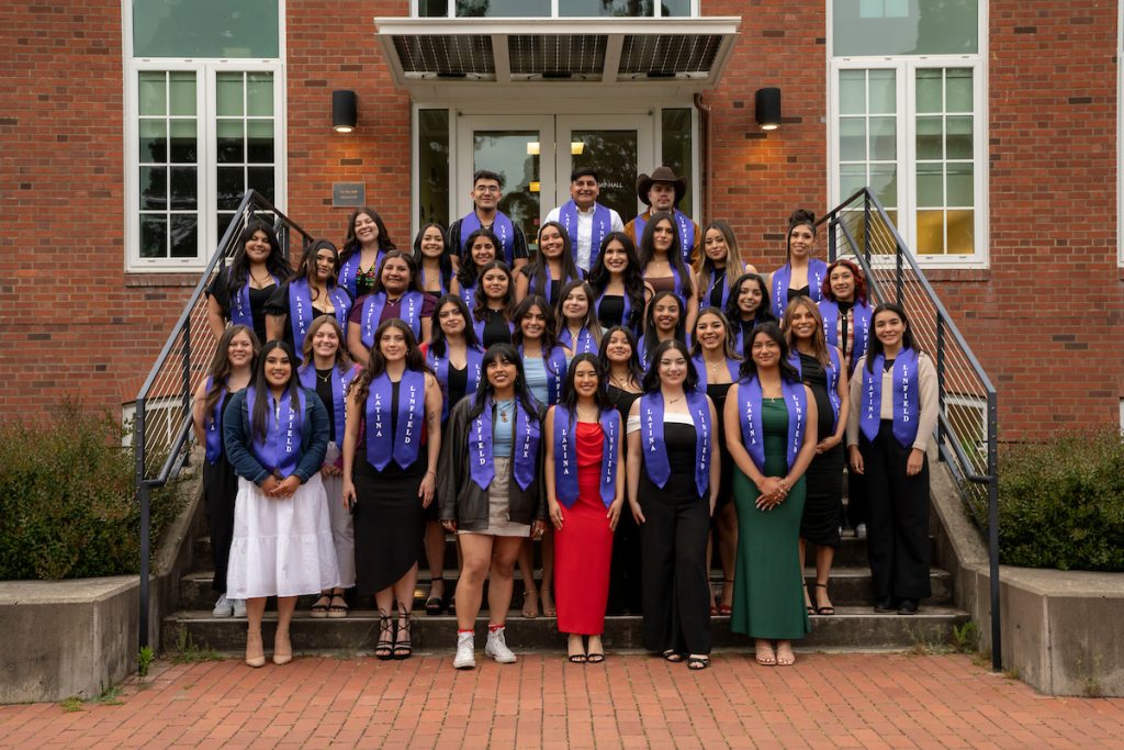 Students pose on the steps of T.J. Day Hall as a group during the Linfield University Latine Dinner; the students wear a purple stole that says ‘Linfield Latino’ or ‘Linfield Latina’.