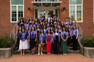 Students pose on the steps of T.J. Day Hall as a group during the Linfield University Latine Dinner; the students wear a purple stole that says ‘Linfield Latino’ or ‘Linfield Latina’.