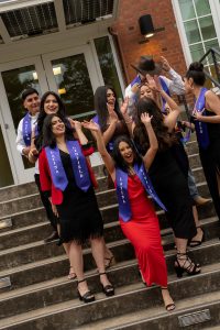 Students cheer on the steps of T.J. Day Hall as a group during the Linfield University Latine Dinner; the students wear a purple stole that says ‘Linfield Latino’ or ‘Linfield Latina’.