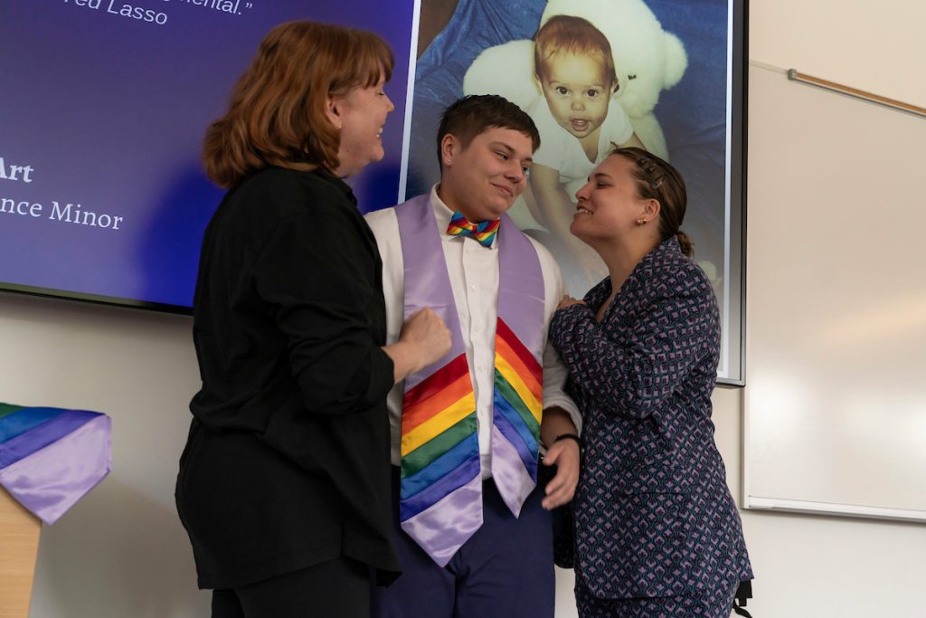 Family members pose next to a graduate during the Linfield University Lavender Celebration; the graduate wears a lavender stole with rainbow trim at the bottom.