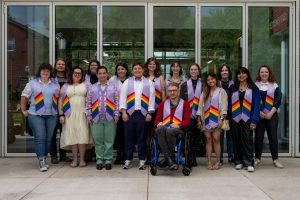 Students wearing lavender stoles with rainbow trim pose as a group in front of Keck Hall at the Linfield University Lavender Celebration.