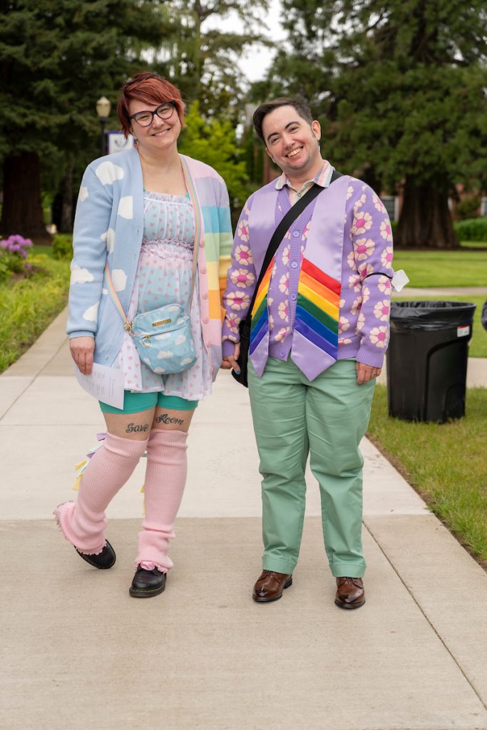 A loved one poses next to a graduate during the Linfield University Lavender Celebration; the graduate wears a lavender stole with rainbow trim at the bottom.