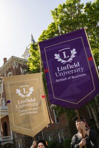 Faculty members hold large banners that say ‘Linfield University School of Business’, “Linfield University College of Arts and Sciences’ and “Linfield University-Good Samaritan School of Nursing’