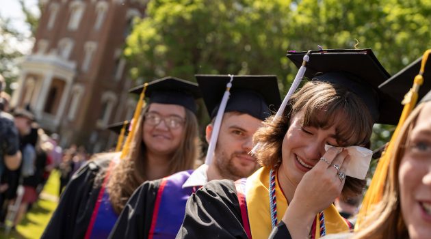Graduates in their gowns and caps are lined up; one wipes away tears