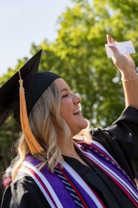 A student dressed in graduation cap and gown smiles during the 2024 Linfield University Commencement.