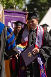 A student holds a diploma and shakes hands with Linfield University’s president during the 2024 Linfield University Commencemen