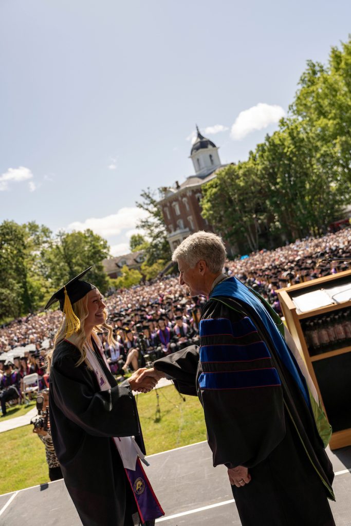 A student holds a diploma and shakes hands with Linfield University’s president during the 2024 Linfield University Commencemen