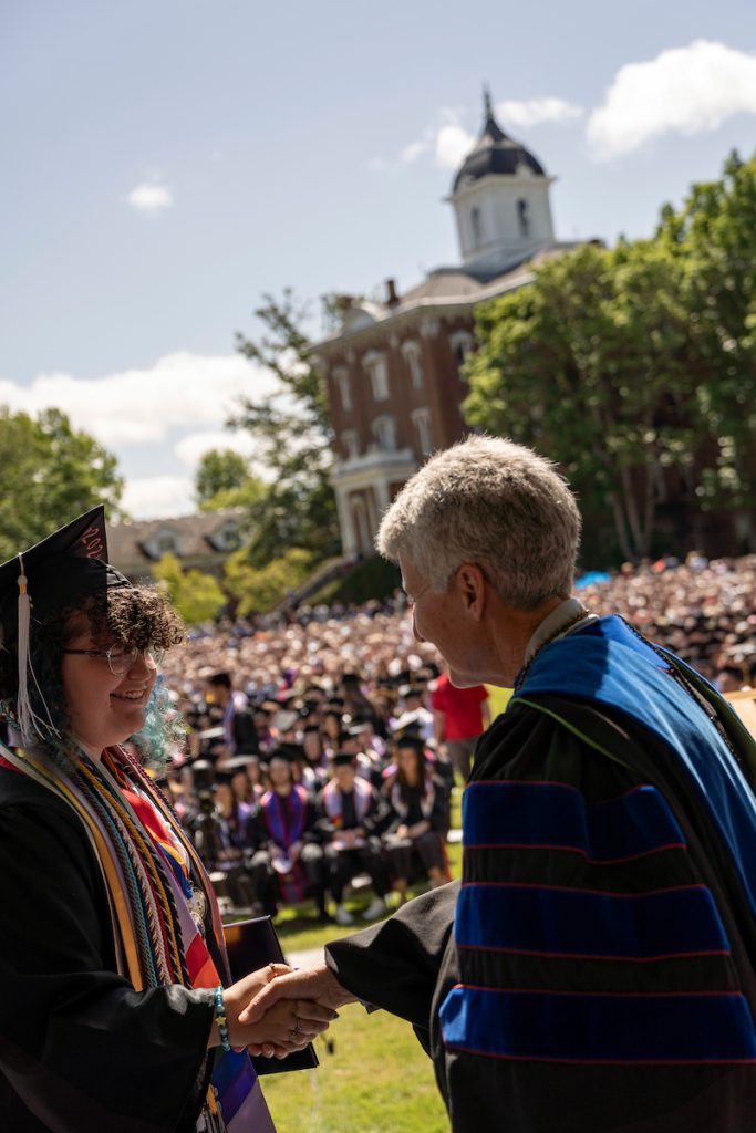 A student holds a diploma and shakes hands with Linfield University’s president during the 2024 Linfield University Commencemen
