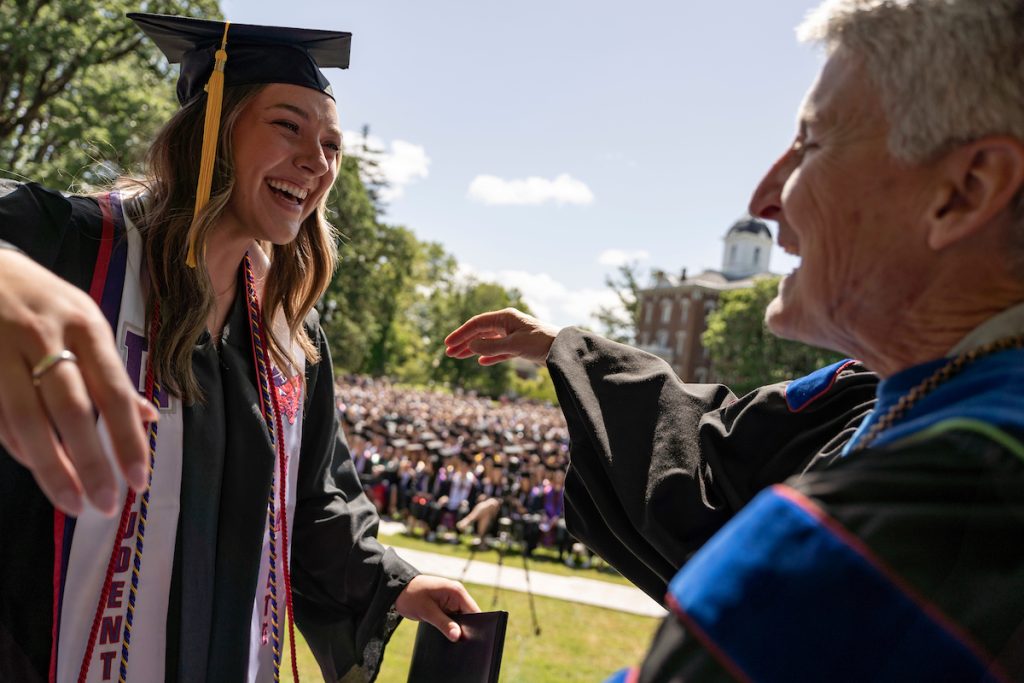 A student holds a diploma and shakes hands with Linfield University’s president during the 2024 Linfield University Commencement.