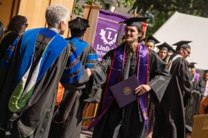 A student holds a diploma and shakes hands with Linfield University’s president during the 2024 Linfield University Commencement.