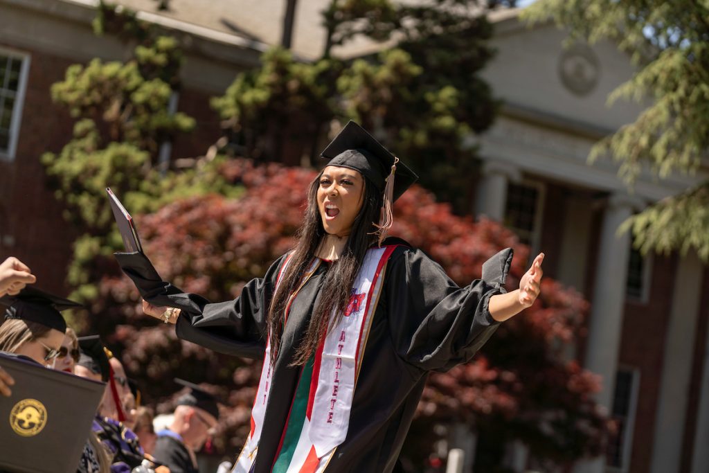 A student poses with their diploma and smiles during the 2024 Linfield University Commencement.