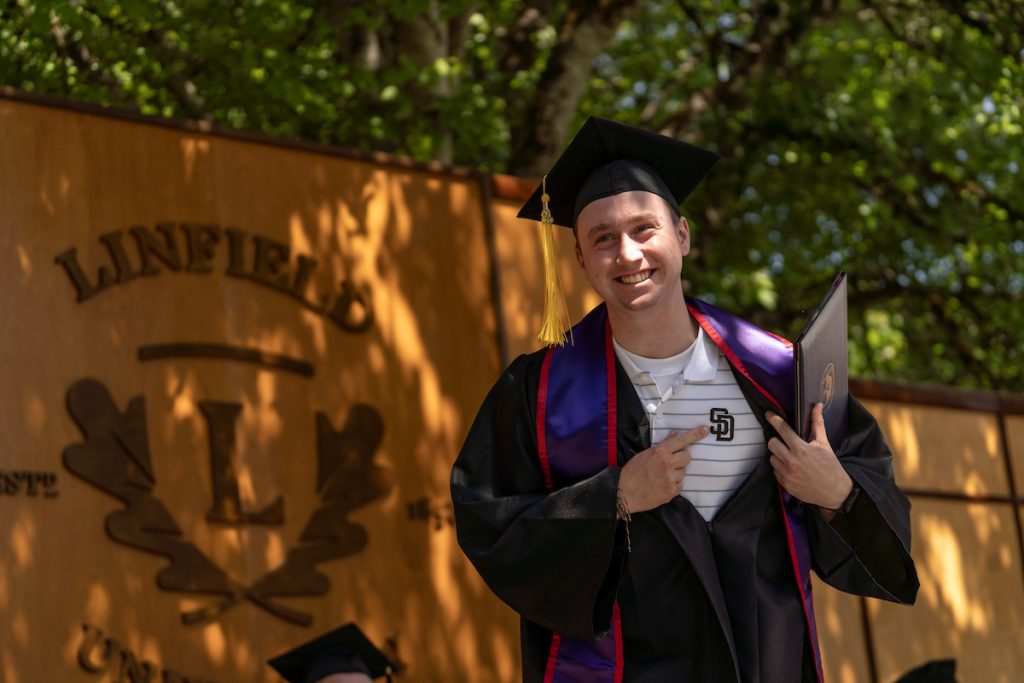A student poses with their diploma and smiles during the 2024 Linfield University Commencement.