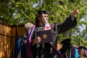 A student poses with their diploma and smiles during the 2024 Linfield University Commencement.