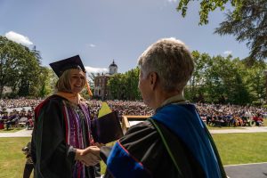 A student holds a diploma and shakes hands with Linfield University’s president during the 2024 Linfield University Commencement.