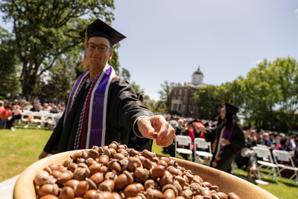 A student places an acorn in a bowl during the 2024 Linfield University Commencement.