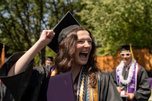 A student poses with their diploma and smiles during the 2024 Linfield University Commencement.