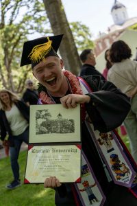 A student poses with their diploma and smiles during the 2024 Linfield University Commencement.