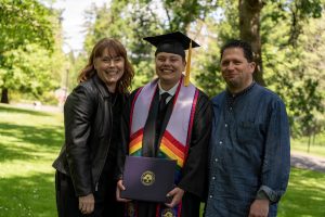 A student poses with their loved ones and smiles during the 2024 Linfield University Commencement.
