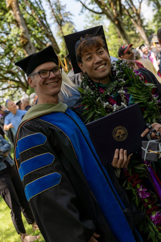 A student poses with a faculty member dressed in academic regalia during the 2024 Linfield University Commencement.