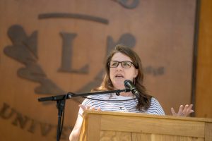 A speaker at the Nurses Pinning ceremony stands at a podium, with a ‘Linfield University’ wooden backdrop behind them.