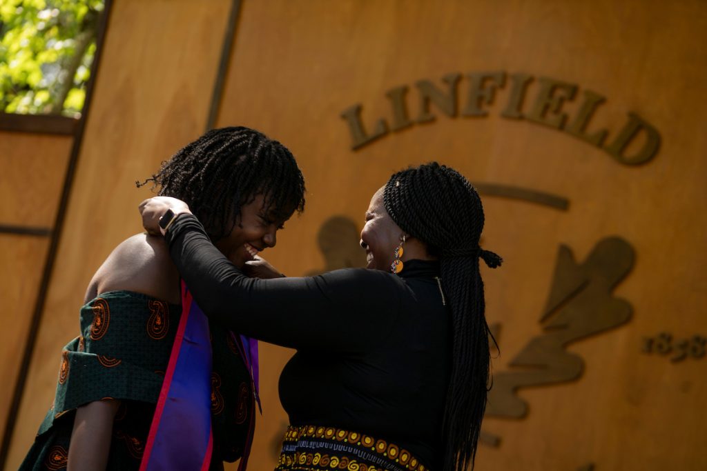 A family member places a purple stole with a red border around the neck of a nursing student graduate.