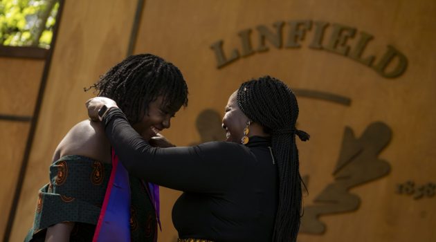 A student smiles as her mother places a purple stole with a Linfield nursing pin around her neck